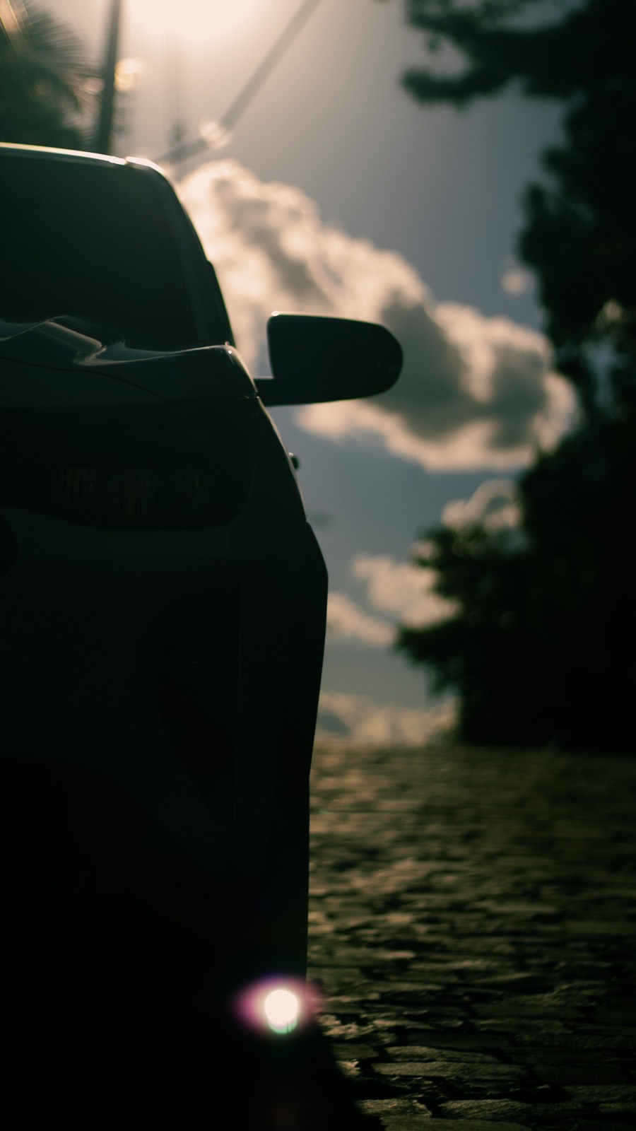 A car in silhouette on a stone road against a luminous sky.