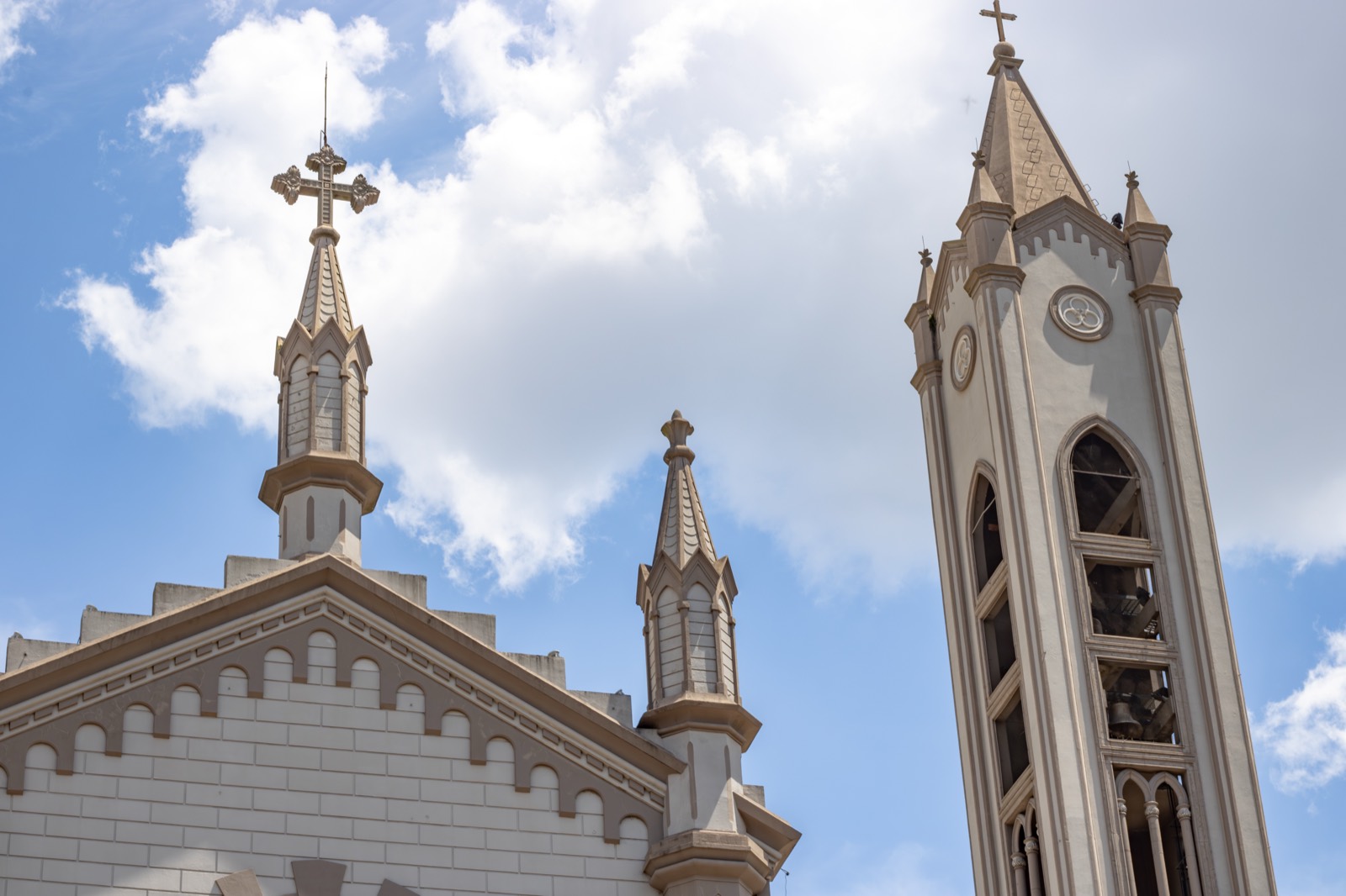 A white church steeple and cross against a bright, cloud-dotted sky.