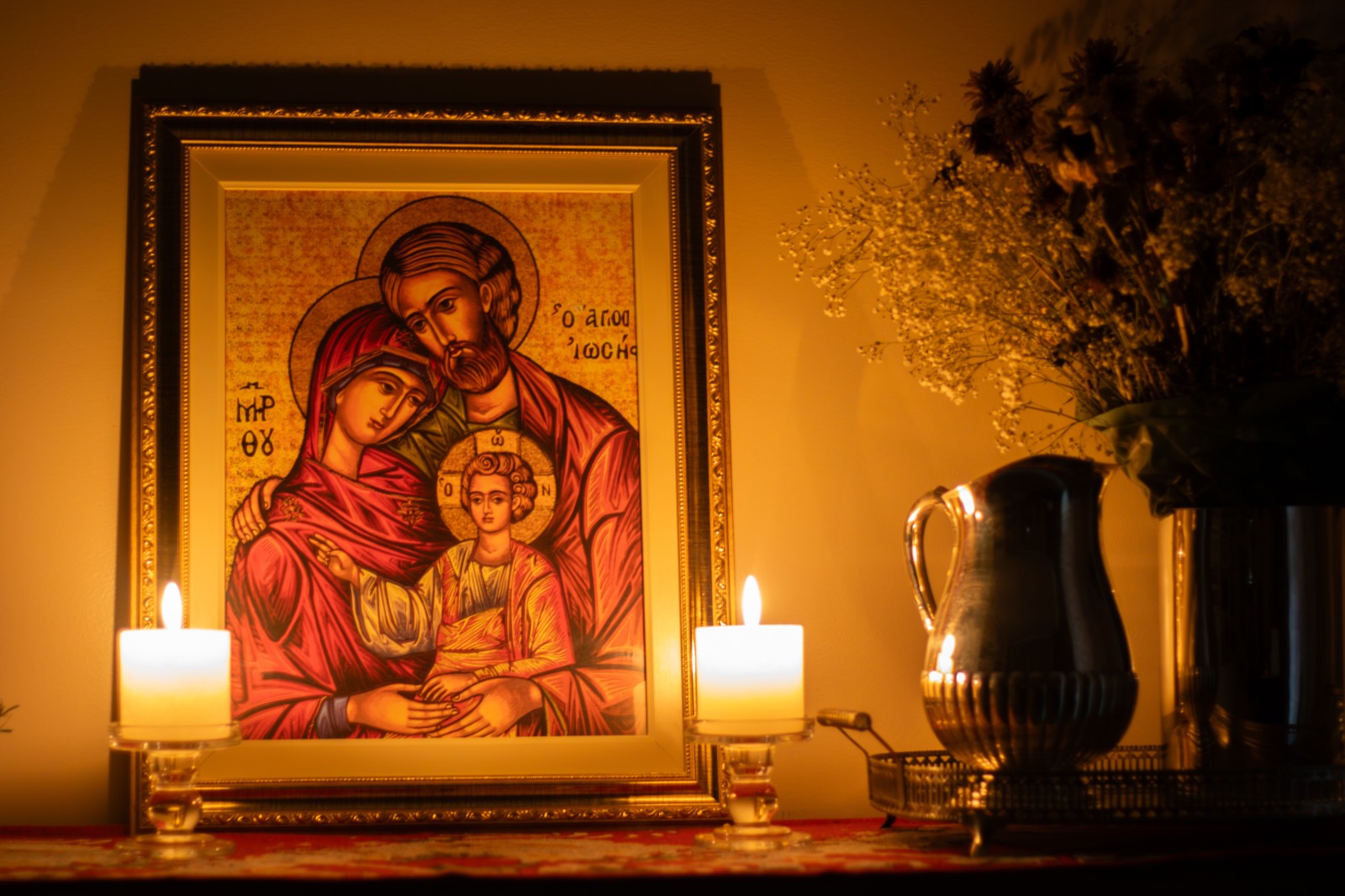 A gilded icon of the Holy Family flanked by two lit candles.