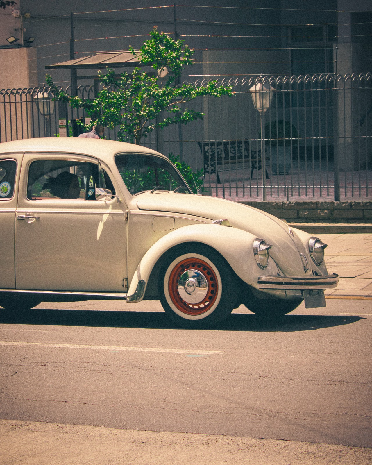 A classic Volkswagen Beetle driving down a street, in vintage tones.