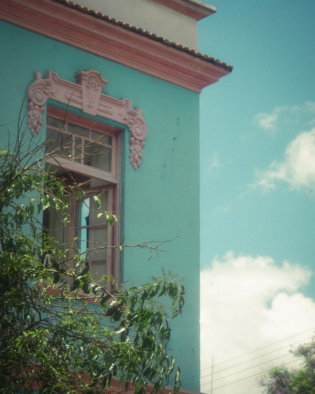 An ornate window on a teal building facade against a blue sky.
