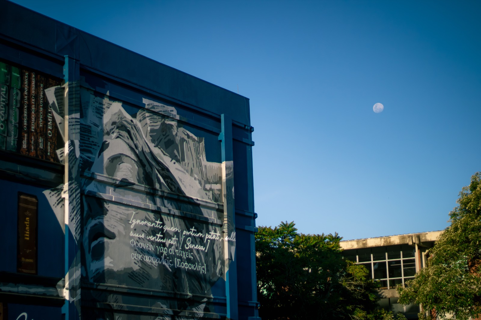 A building at dusk with a painted mural and the moon overhead.